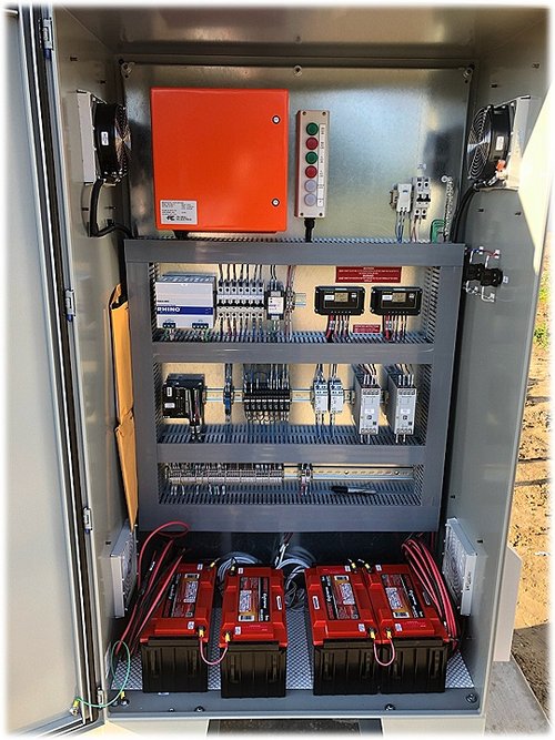 An electrical control panel with wiring, circuit breakers, electronic modules, and four red batteries at the bottom—ideal for Products - Rural Electric applications.