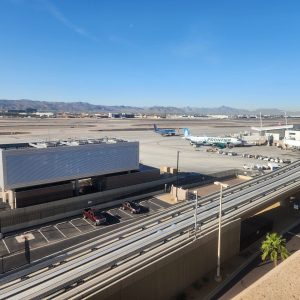 A Frontier airplane is parked at an airport gate near runways, with mountains and signs of past mining activity in the background, and elevated roads in the foreground. A Frontier airplane is parked at an airport gate near runways, with mountains and signs of past mining activity in the background, and elevated roads in the foreground.