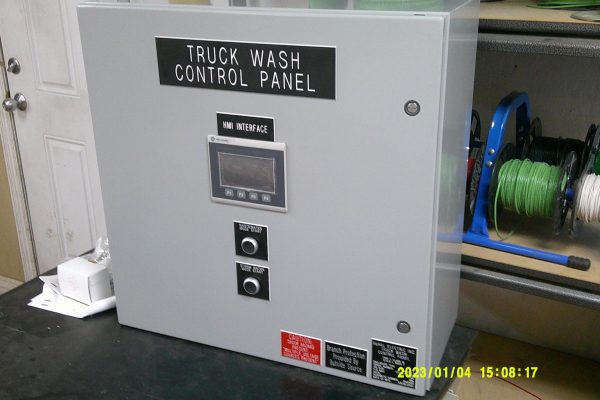 Gray metal truck wash control panel with digital display and two buttons, set on a black surface near a shelf holding spools of wire—ideal for Home – Rural Electric setups. Gray metal truck wash control panel with digital display and two buttons, set on a black surface near a shelf holding spools of wire—ideal for Home - Rural Electric setups.