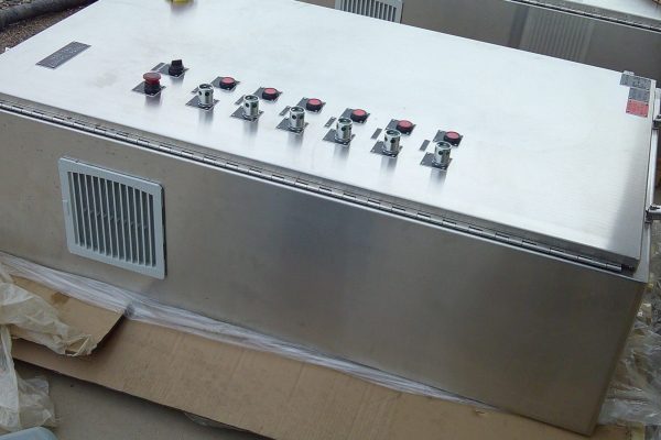 A metal electrical control panel designed for rural electric applications, featuring a ventilation grill, several toggle switches, and red push buttons on top, placed on cardboard outdoors—ideal for manufacturing environments. A metal electrical control panel designed for rural electric applications, featuring a ventilation grill, several toggle switches, and red push buttons on top, placed on cardboard outdoors—ideal for manufacturing environments.