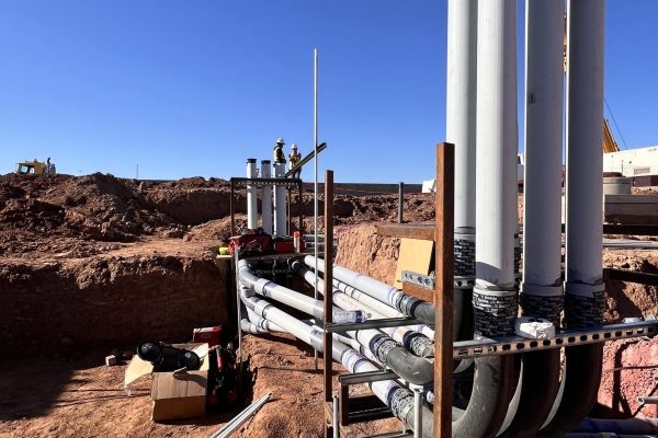 Workers stand on an industrial excavation site, installing multiple large white conduit pipes vertically and horizontally—essential infrastructure for a rural electric project; construction tools and materials are nearby. Workers stand on an industrial excavation site, installing multiple large white conduit pipes vertically and horizontally—essential infrastructure for a rural electric project; construction tools and materials are nearby.