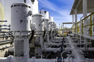 A row of large industrial pumps labeled P-1, P-2, and P-3, connected to pipes in an outdoor facility with metal railings and a covered walkway. A row of large industrial pumps labeled P-1, P-2, and P-3, connected to pipes in an outdoor facility with metal railings and a covered walkway.